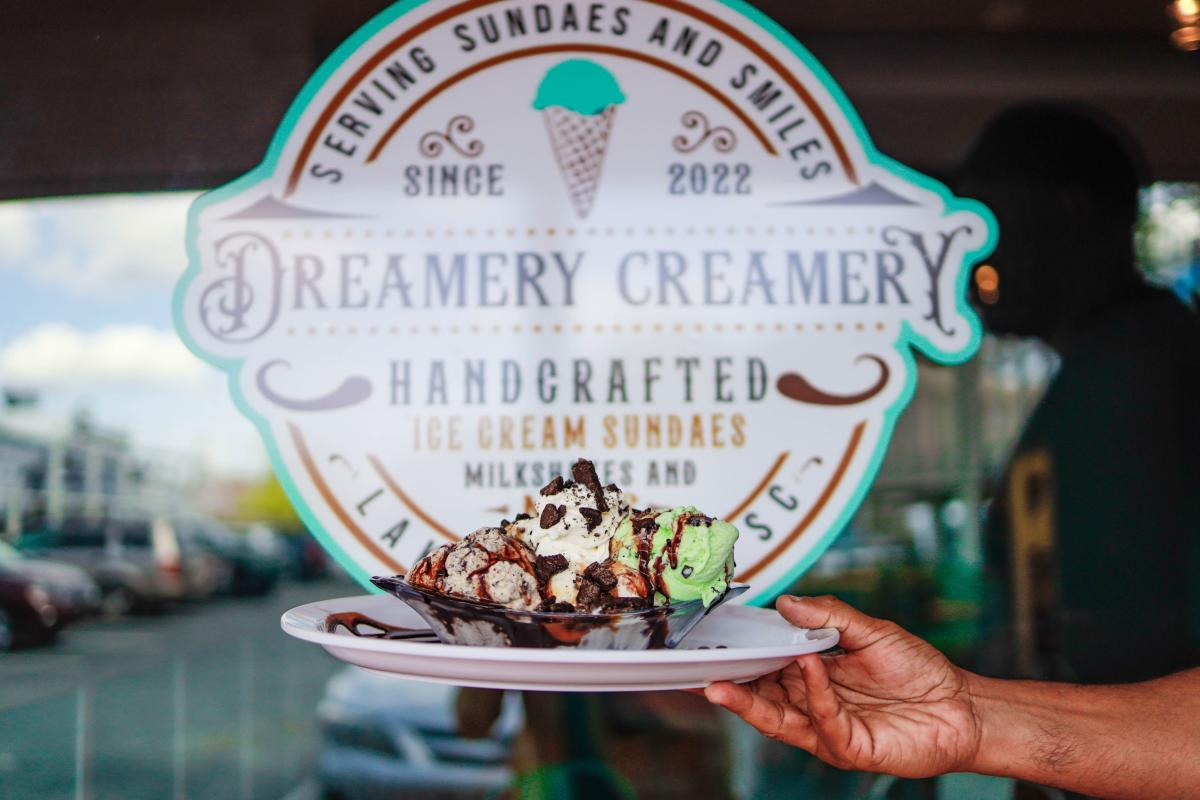 A hand holding a plate of ice cream in front of the Dreamery Creamery store in Lake Wylie, SC